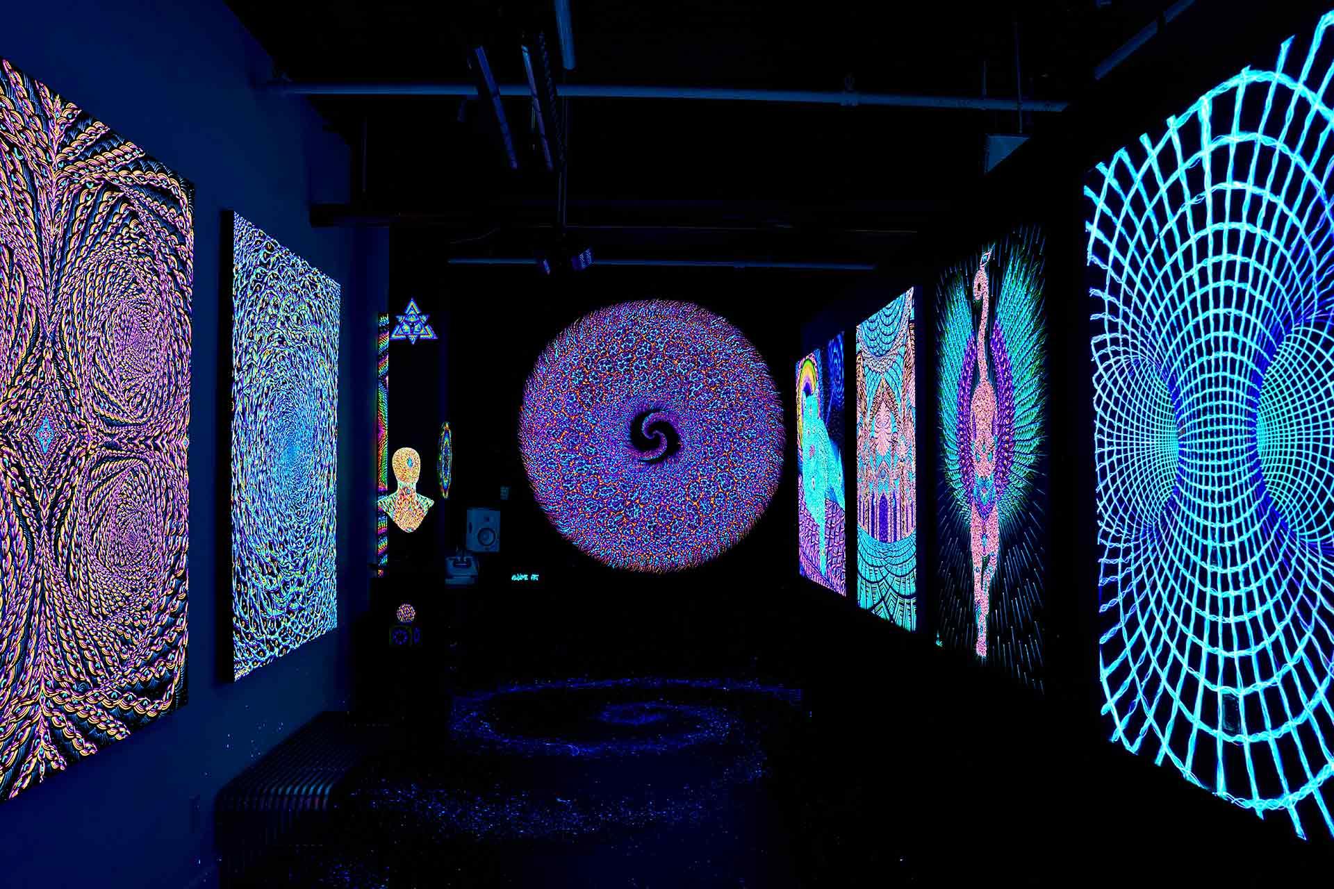 A dark room features glowing, psychedelic art on the walls, including intricate patterns, mandalas, a central circular art piece with a spiral design, and vibrant blue, purple, and neon colors throughout.
