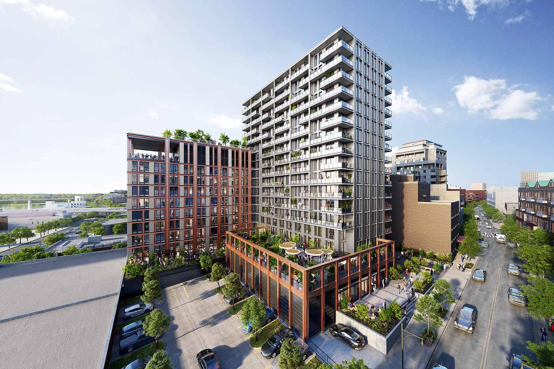 Aerial view of a modern apartment complex with multiple mid-rise buildings, rooftop gardens, balconies, and a central courtyard, surrounded by trees and city streets under a blue sky.