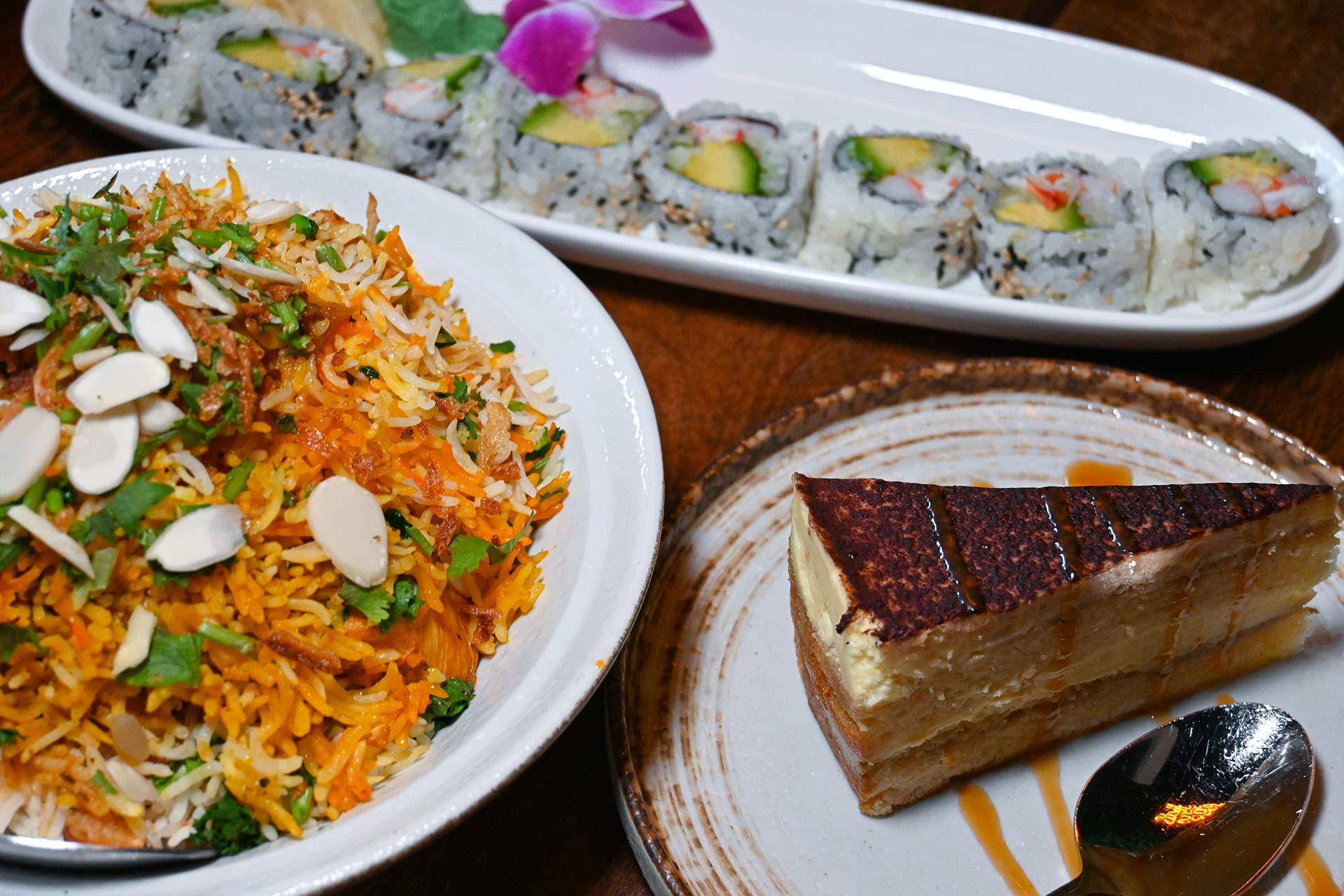 A plate of biryani garnished with sliced almonds and herbs, a platter of sushi rolls with avocado and crab, and a slice of layered tiramisu cake with a spoon on the side.