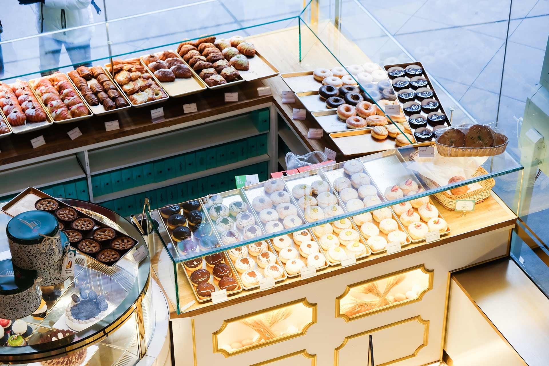 A bakery display filled with assorted pastries, donuts, and baked goods arranged neatly on trays behind glass, with cakes and desserts visible on the counter.